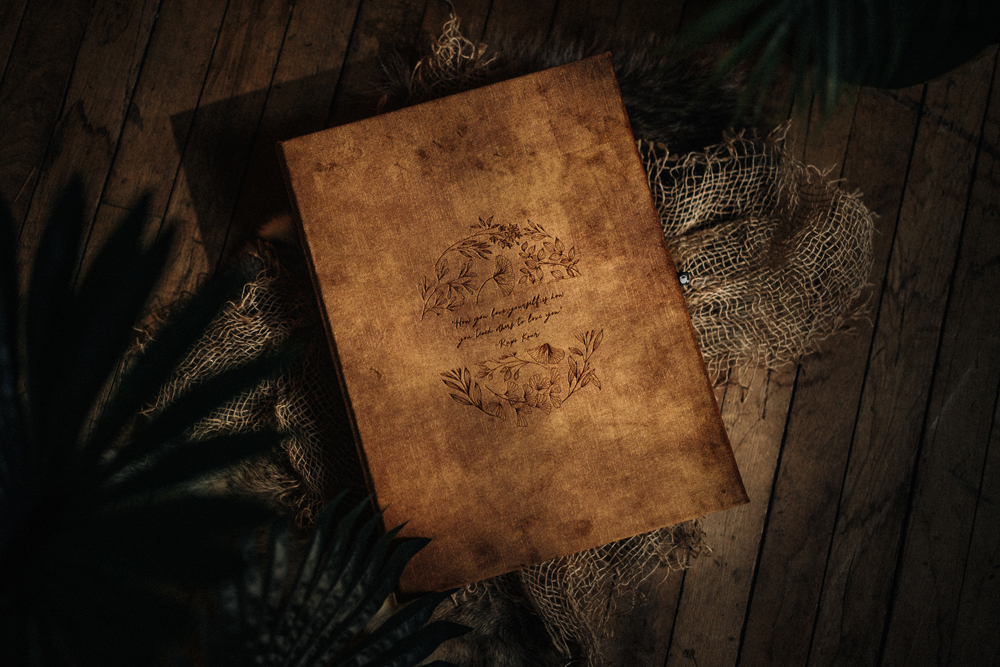 Luxury leather boudoir photo album with engraved cover design displayed on a rustic wooden surface with soft decorative textures.