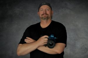 Chris Davis, owner and lead photographer of Primal Soul Boudoir, stands holding a Nikon camera during a professional branding session near Houston, Texas.