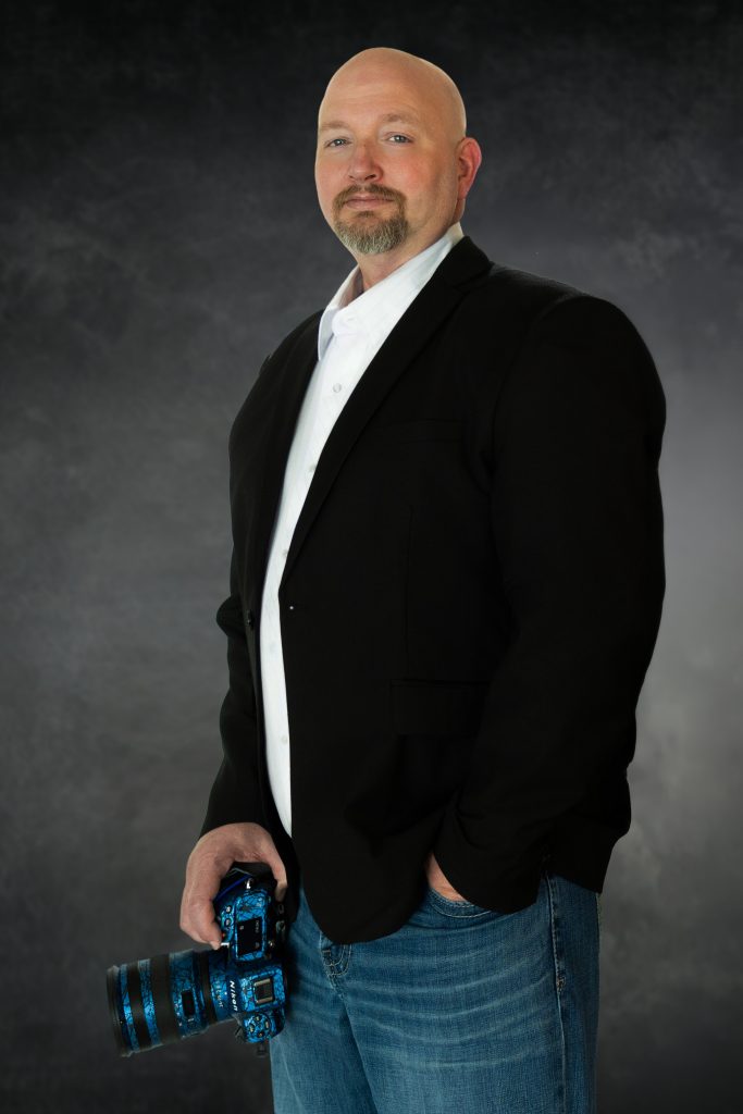 Chris Davis, owner of Primal Soul Boudoir, stands in a blazer and jeans holding a Nikon camera during a professional branding session near Houston, Texas.