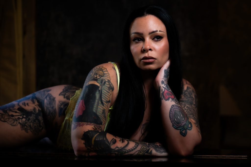 Luxury boudoir portrait of a tattooed woman in delicate lace lingerie, showcasing artistic body art and confident expression during a Houston boudoir photography session.