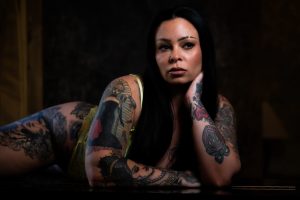 Luxury boudoir portrait of a tattooed woman in delicate lace lingerie, showcasing artistic body art and confident expression during a Houston boudoir photography session.