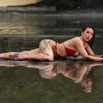 Woman posing in shallow water wearing a red bikini during an adventurous outdoor mud boudoir photography session near Houston, Texas.