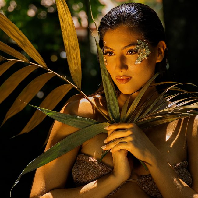 A woman with botanical-inspired makeup poses among tropical palm leaves in an editorial boudoir portrait during a luxury boudoir session near Houston, Texas.
