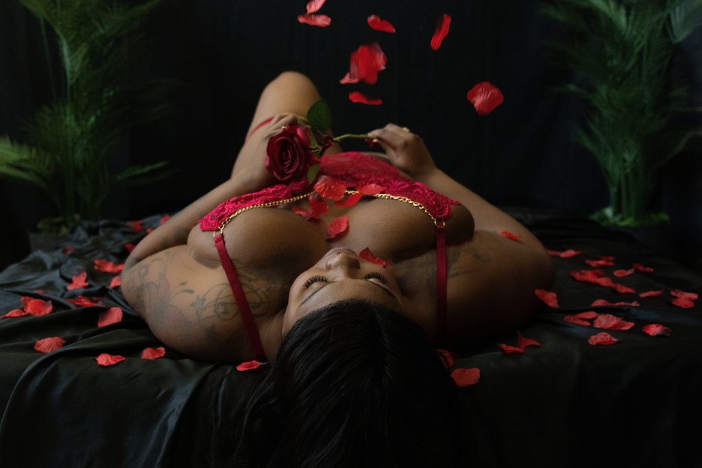 Woman in red lingerie surrounded by falling rose petals during a luxurious Valentine's Day boudoir photoshoot in Houston.