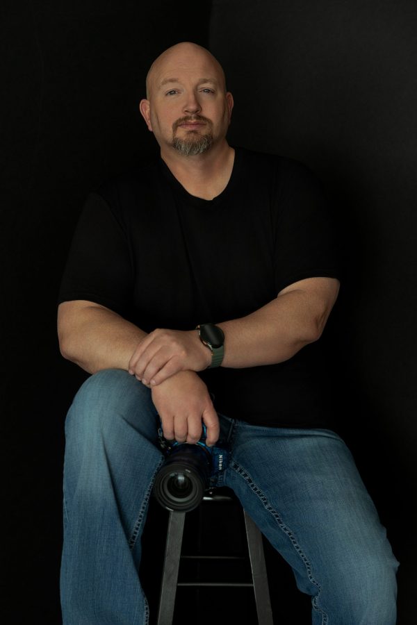 Chris Davis, owner and photographer of Primal Soul Boudoir, sits holding a Nikon camera during a branding portrait session near Houston, Texas.