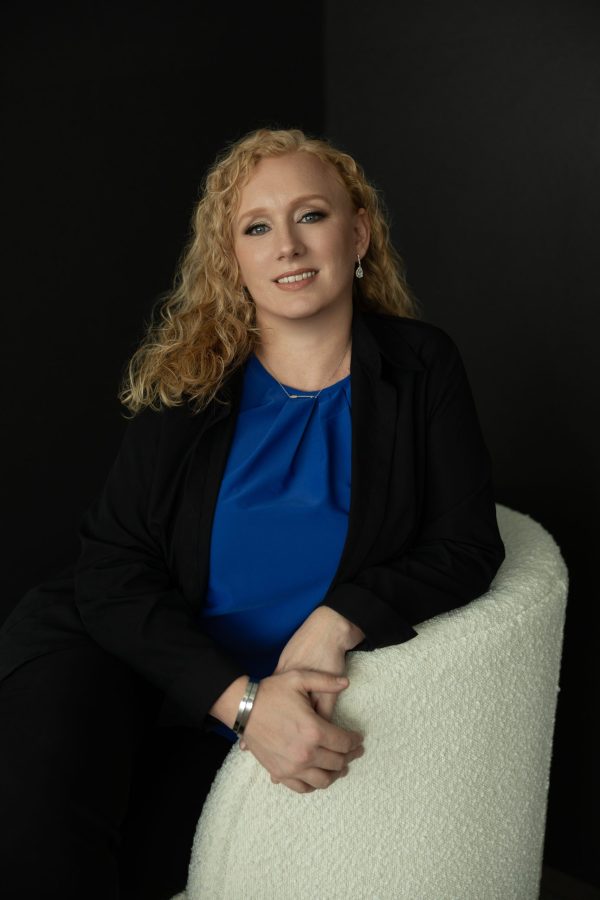 Heidi Fritsche, co-owner of Primal Soul Boudoir, sits in a white chair wearing a blue blouse and black blazer during a branding session near Houston, Texas.